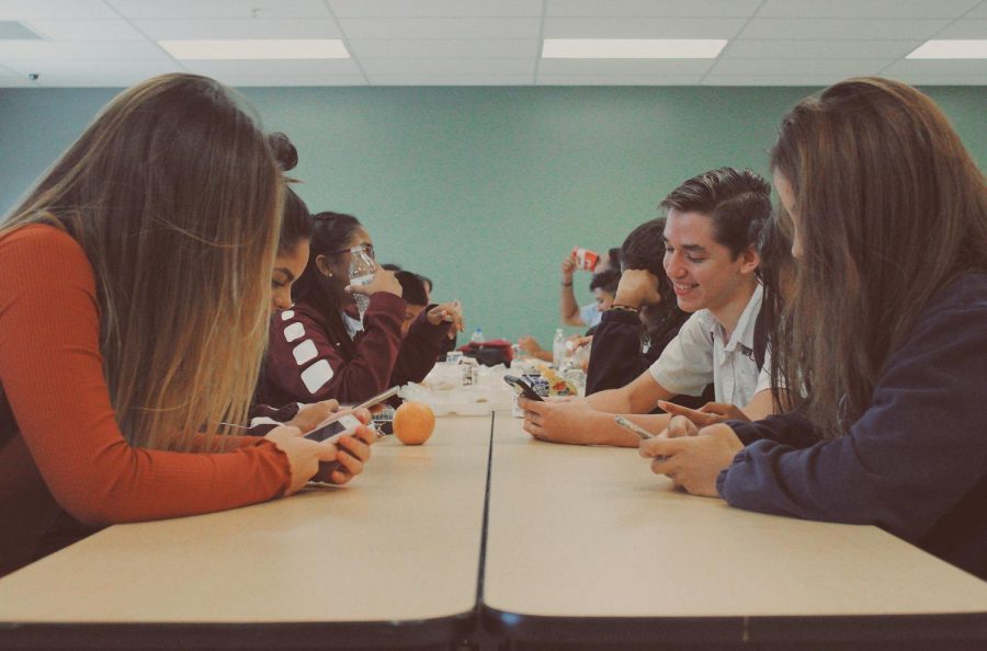 Students at lunch busy on their phones rather than socializing in person.