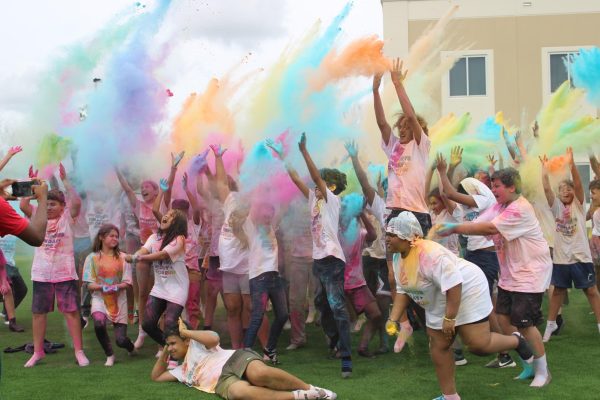 Color run participants celebrate and  throw colored powder in the air.