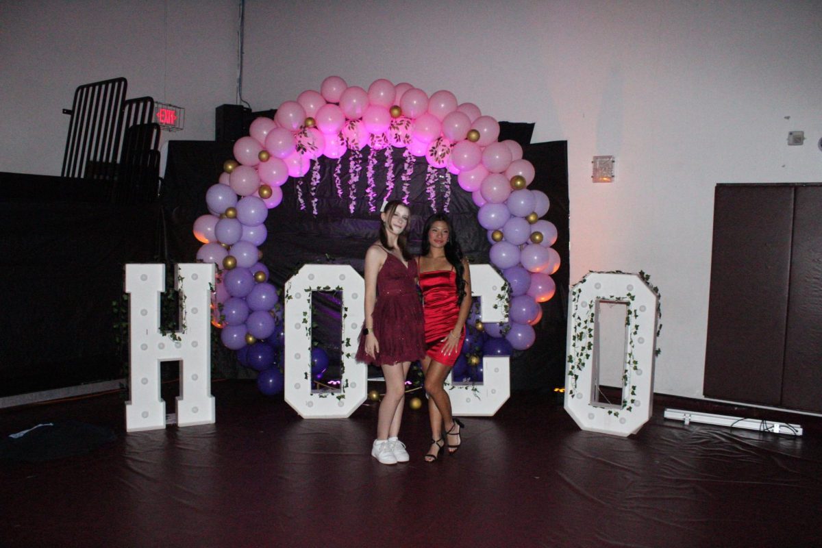 Senior Mia Villanueva posing with friend, Senior Madeline Seaman in front of the HOCO sign.