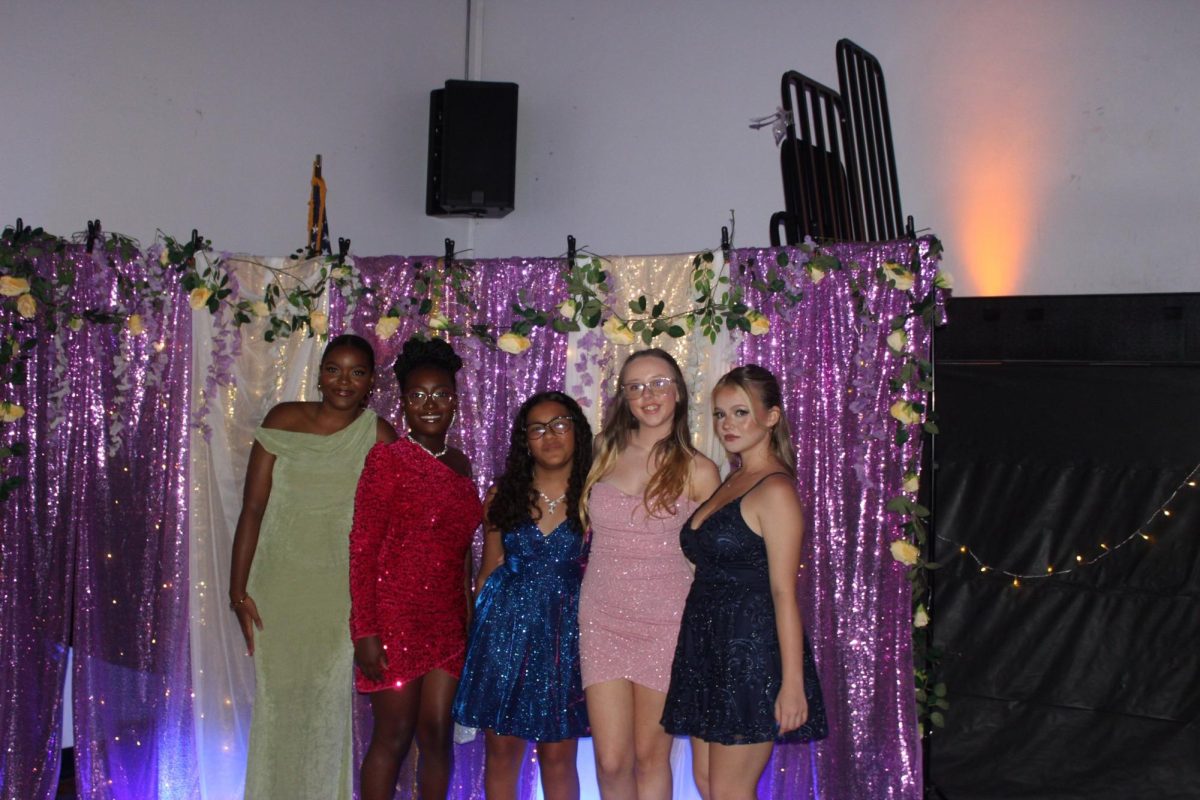 Freshmen Kailey Rose posing with friends in front of Homecoming decorations.