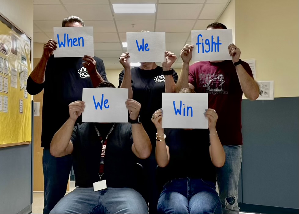 Teacher's pose behind a paper that reads of a Democratic slogan. 